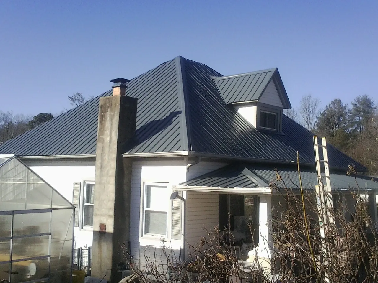 Dark blue standing seam metal roof on a white farmhouse with dormer — Slate & Tile Roof Repair by Roofing Brothers in Colt