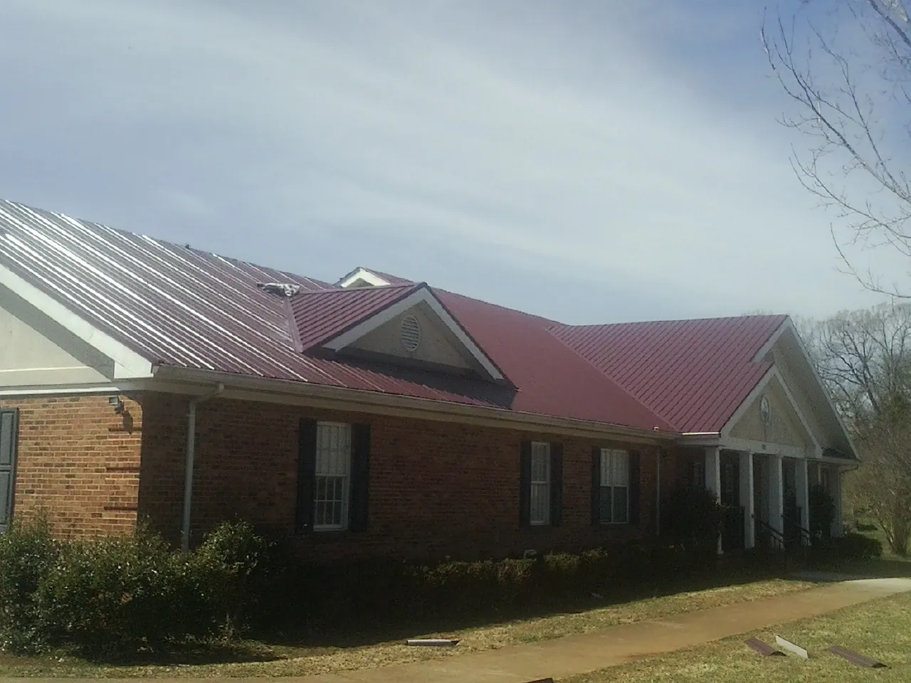 Red metal roof with gabled entries on a long brick building, from a Hail Damage Roof Repair job in Colt