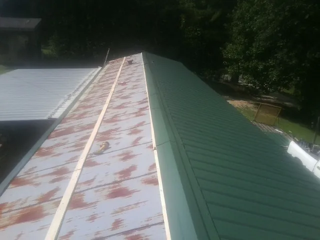 Old rusted panels beside newly installed green metal roofing — Wind Damage Roof Repair by Roofing Brothers in Colt