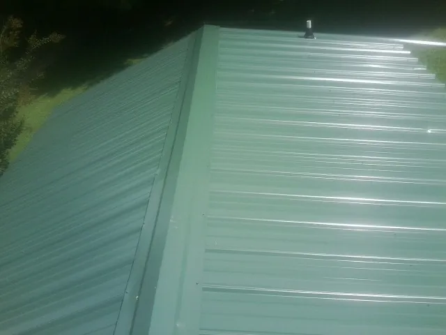 New green metal panels meeting at the ridge of a roof — Flat Roof Repair work by our crew in Colt