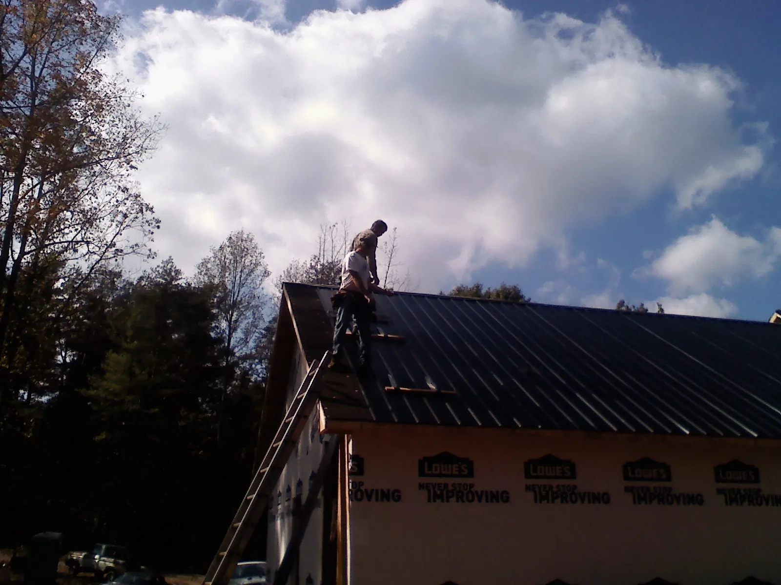 Roofer fastening dark metal panels high against a cloudy sky, from a Roof Inspection job in Colt