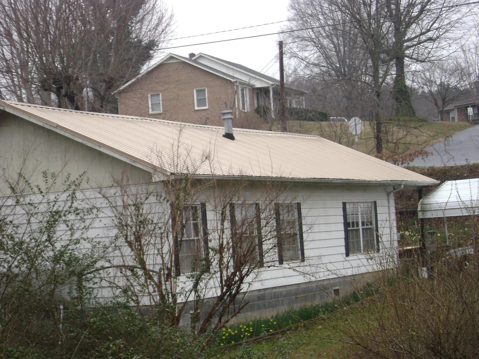 Tan metal roof on a white sided house set into a hillside — Commercial Roofing by Roofing Brothers in Colt