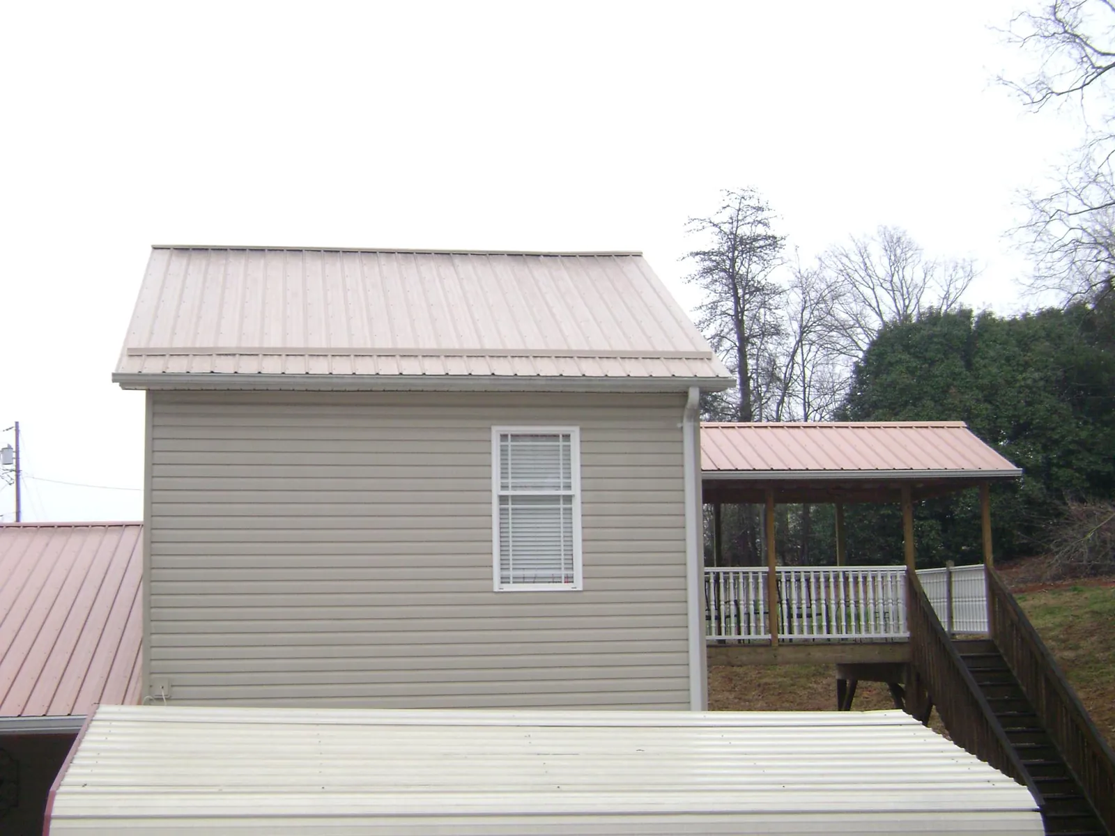 Tan metal roofs on a two story addition and attached porch, from a Roof Replacement job in Colt