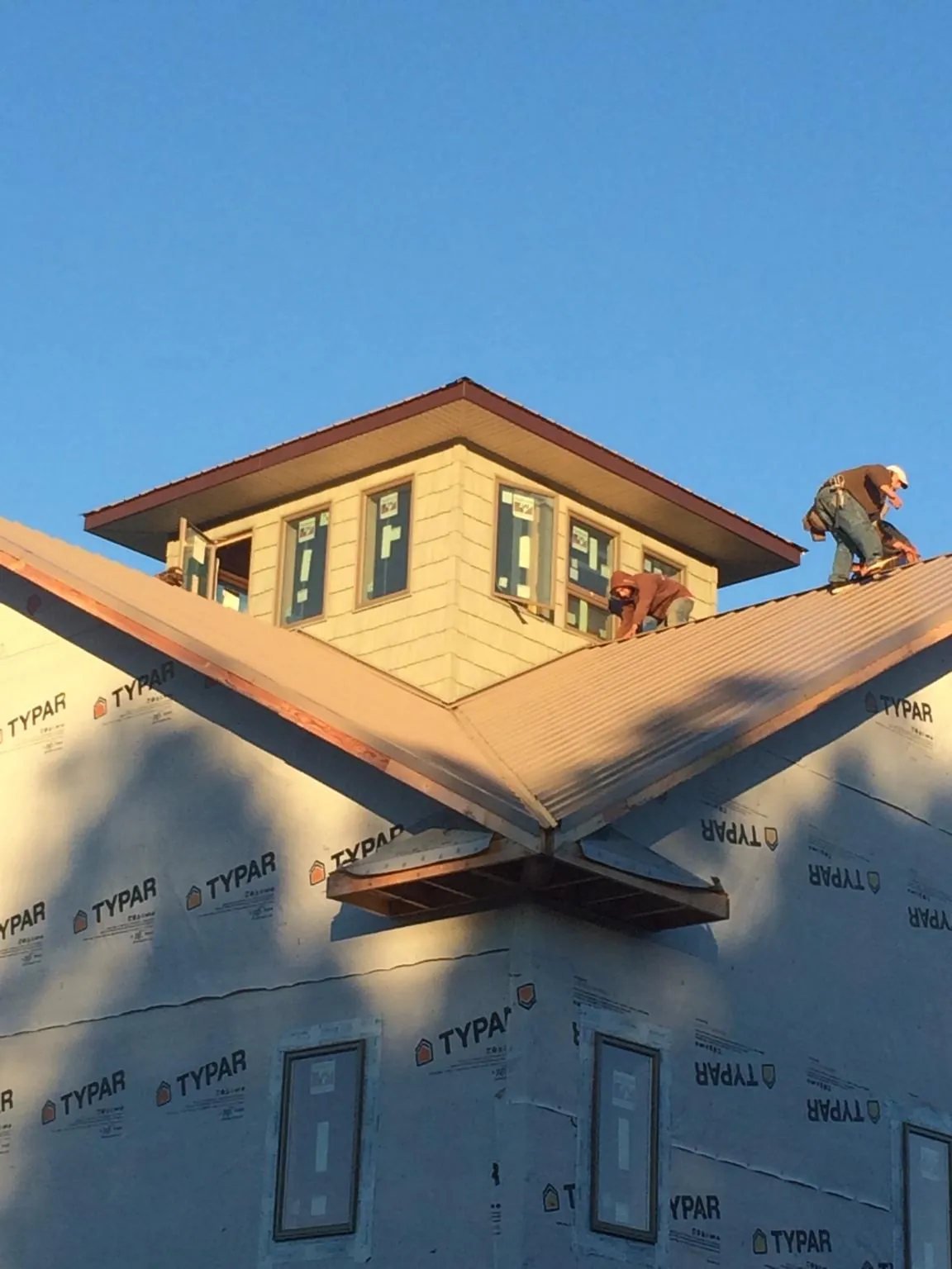 Roofers working around a rooftop cupola on a new metal roof at sunset — Roof Waterproofing in Colt by Roofing Brothers